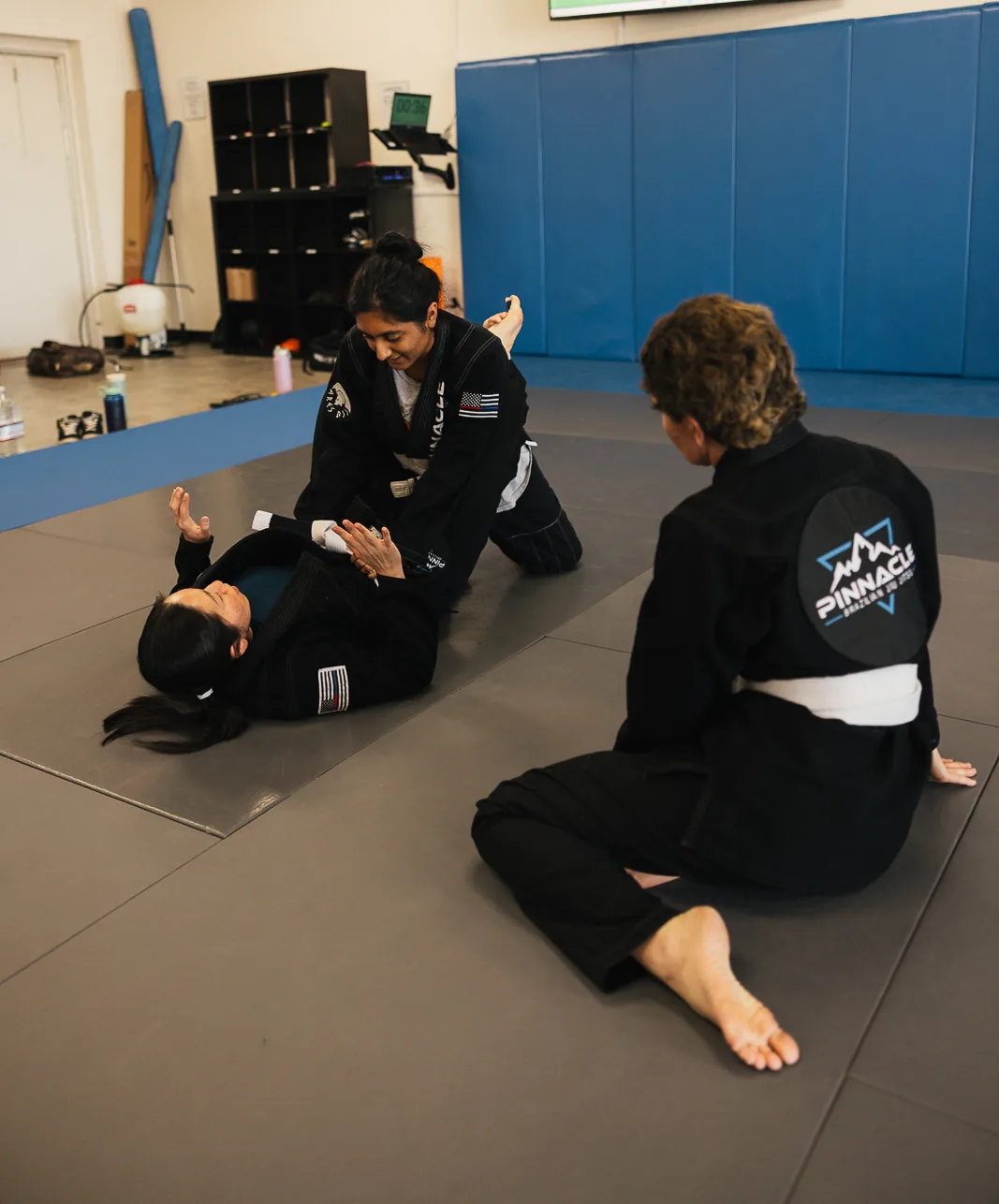 A coach guiding two students through a self-defense drill during the women&rsquo;s class at Pinnacle Brazilian Jiu Jitsu